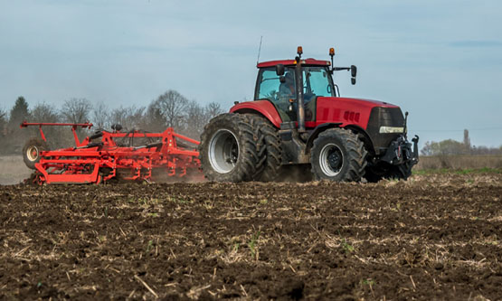 Rød traktor der harver den sorte jord på en mark